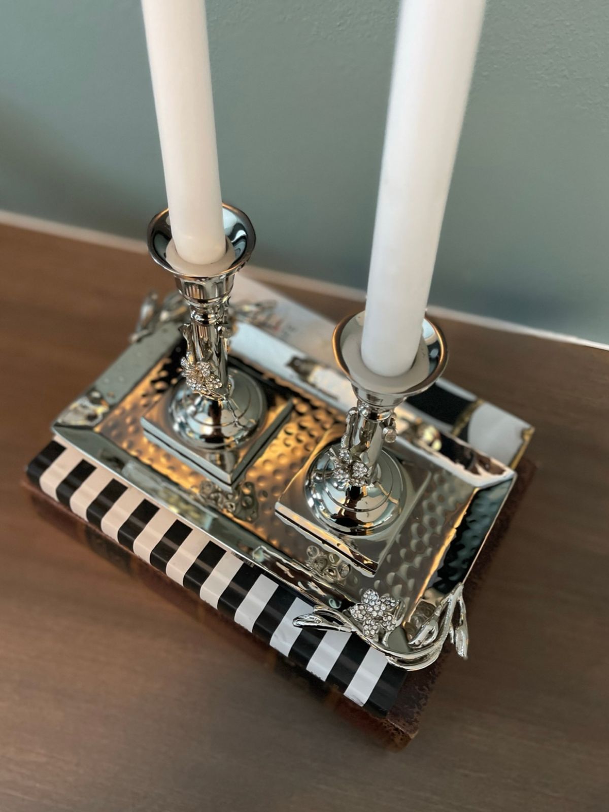 Stainless steel candle holder set with hammered finish displayed on a credenza atop a book, showcasing jeweled flower details for an elegant home decor look.